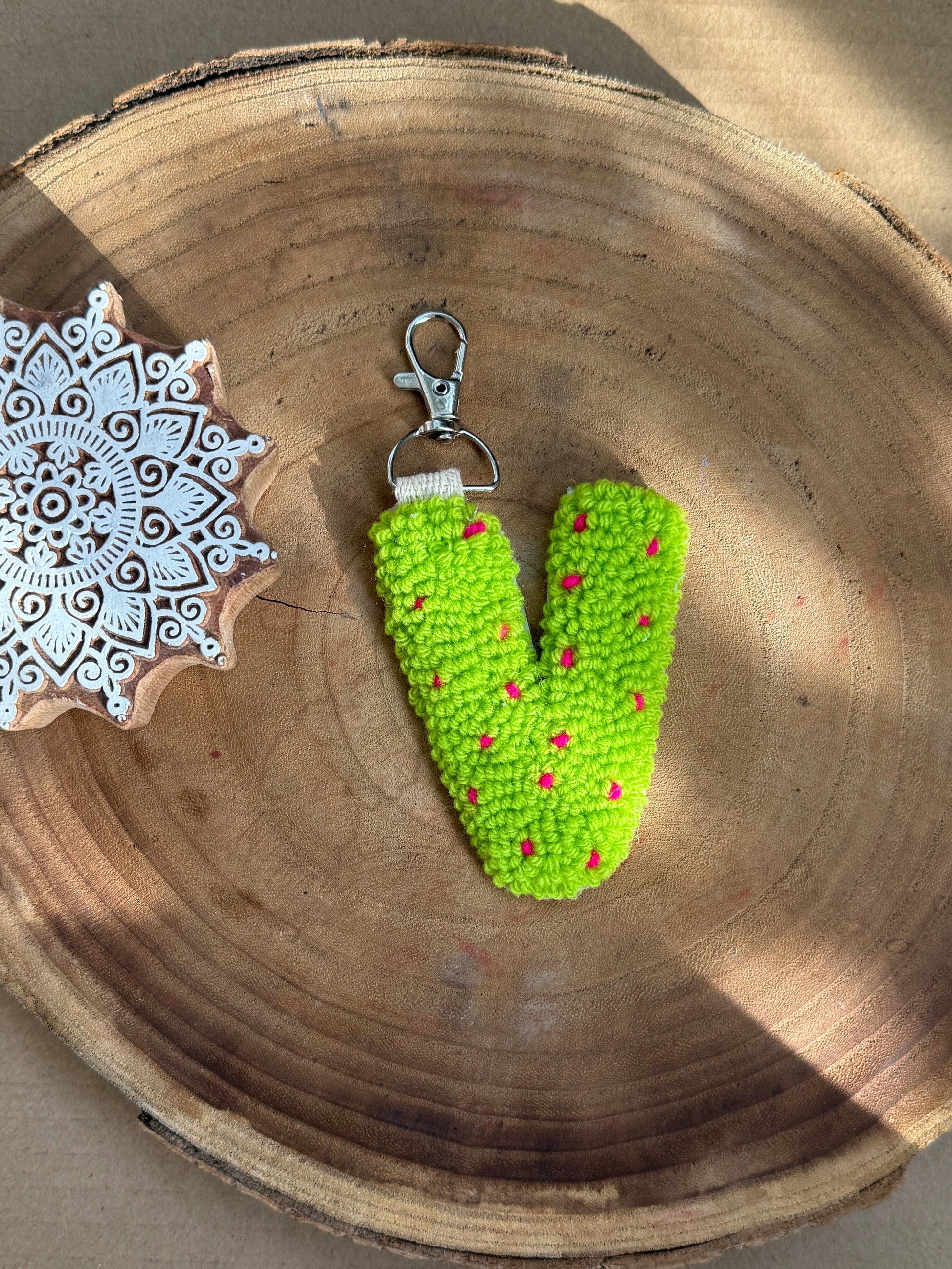 A bright green Punch Needle letter 'V' keychain with small red speckled accents and a silver lobster clasp